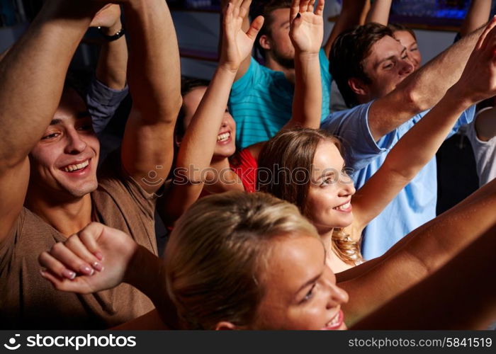 party, holidays, celebration, nightlife and people concept - group of smiling friends waving hands at concert in club