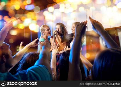 party, holidays, celebration, nightlife and people concept - happy young women singing karaoke in night club behind crowd of music fan