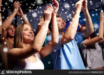 party, holidays, celebration, nightlife and people concept - smiling friends applauding at concert in club and snow effect