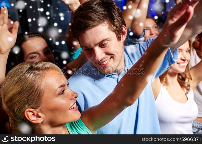 party, holidays, celebration, nightlife and people concept - smiling friends waving hands at concert in club and snow effect