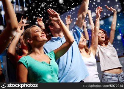 party, holidays, celebration, nightlife and people concept - smiling friends waving hands at concert in club and snow effect