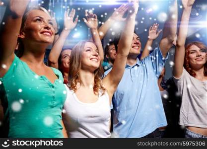 party, holidays, celebration, nightlife and people concept - smiling friends waving hands at concert in club and snow effect