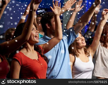 party, holidays, celebration, nightlife and people concept - smiling friends waving hands at concert in club and snow effect