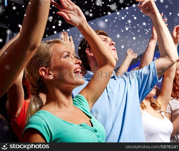 party, holidays, celebration, nightlife and people concept - smiling friends waving hands at concert in club and snow effect