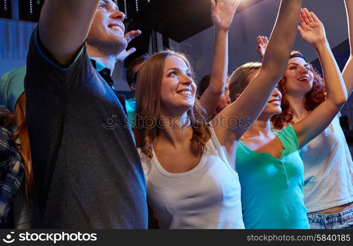 party, holidays, celebration, nightlife and people concept - smiling friends waving hands at concert in club