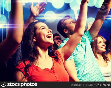 party, holidays, celebration, nightlife and people concept - smiling friends waving hands at concert in club