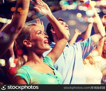 party, holidays, celebration, nightlife and people concept - smiling friends waving hands at concert in club