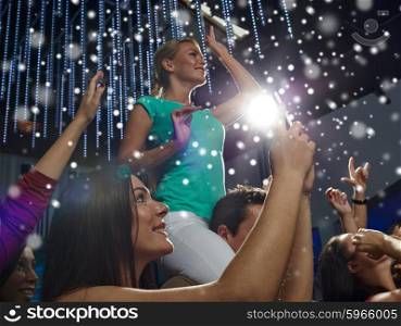 party, holidays, celebration, nightlife and people concept - smiling friends with smartphone taking picture and waving hands at concert in club and snow effect