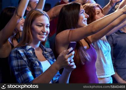 party, holidays, celebration, nightlife and people concept - smiling young woman with smartphone texting message at concert in club