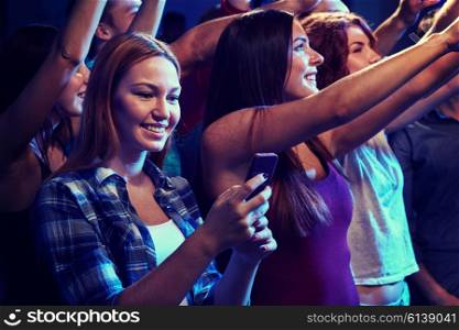 party, holidays, celebration, nightlife and people concept - smiling young woman with smartphone texting message at concert in club