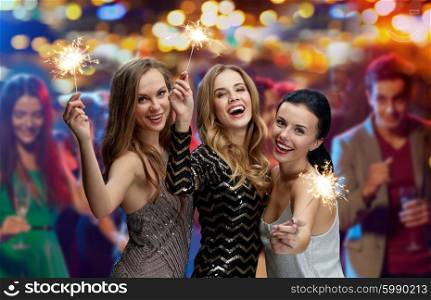 party, holidays, nightlife and people concept - happy young women with sparklers at night club over lights background