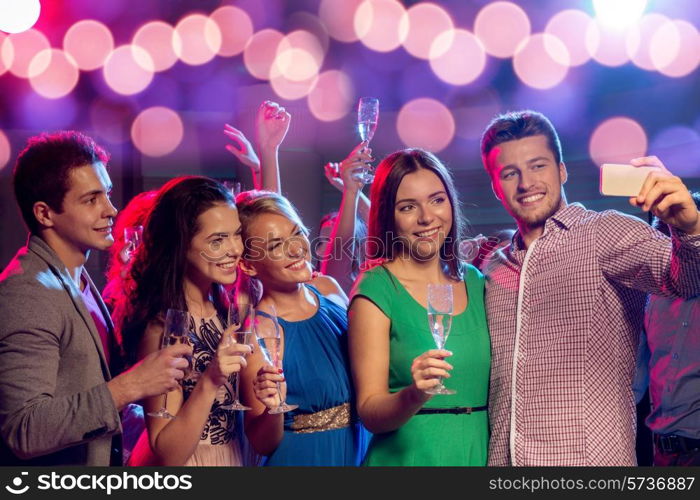 party, holidays, technology, nightlife and people concept - smiling friends with glasses of champagne and smartphone taking selfie in club