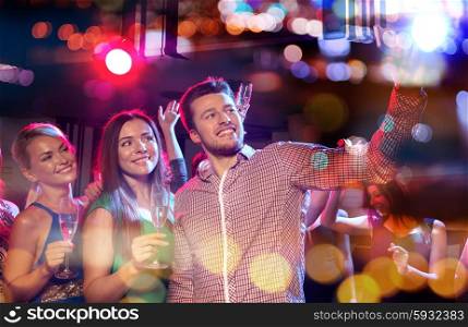 party, holidays, technology, nightlife and people concept - smiling friends with glasses of champagne and smartphone taking selfie in night club with holidays lights