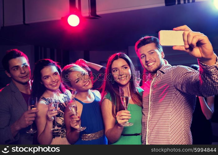 party, holidays, technology, nightlife and people concept - smiling friends with glasses of champagne and smartphone taking selfie in club