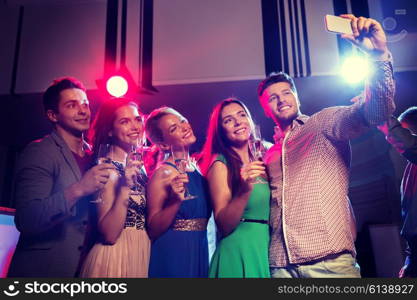 party, holidays, technology, nightlife and people concept - smiling friends with glasses of champagne and smartphone taking selfie in club