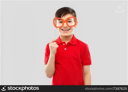 party props, photo booth and childhood concept - smiling little boy in red polo t-shirt with big paper glasses over grey background. smiling boy in red t-shirt with big paper glasses