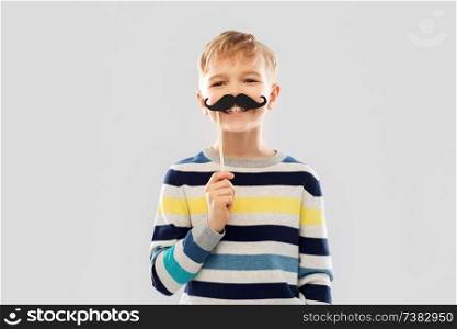 party props, photo booth and childhood concept - smiling little boy with black vintage moustaches over grey background. smiling boy with black vintage moustaches