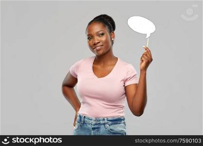 party props, photo booth and communication concept - happy african american young woman holding blank speech bubble over grey background. happy african american woman holding speech bubble