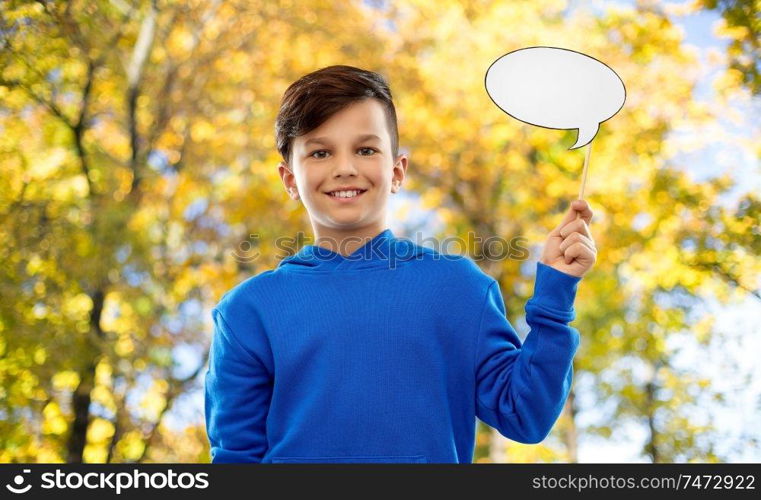 party props, photo booth and communication concept - smiling boy in blue hoodie holding blank speech bubble over autumn park background. smiling boy in blue hoodie with speech bubble