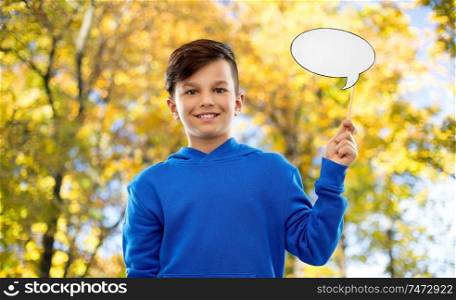 party props, photo booth and communication concept - smiling boy in blue hoodie holding blank speech bubble over autumn park background. smiling boy in blue hoodie with speech bubble