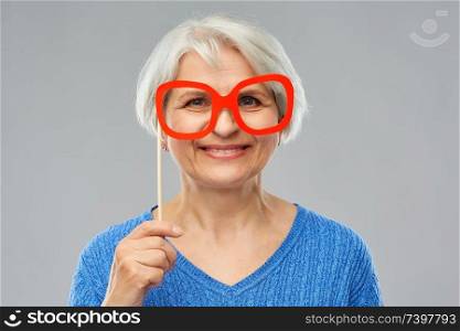 party props, photo booth and old people concept - portrait of smiling senior woman in blue sweater with big glasses over grey background. funny senior woman with big party glasses