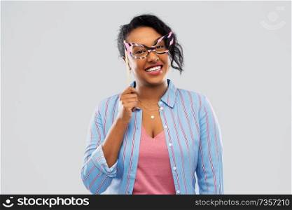 party props, photo booth and people concept - happy african american young woman with big glasses over grey background. happy african american woman with big glasses