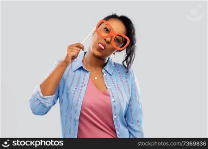 party props, photo booth and people concept - happy african american young woman with big glasses showing tongue over grey background. happy african american woman with big glasses