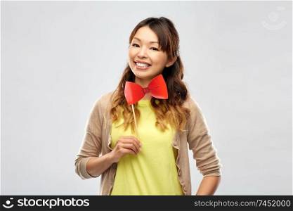 party props, photo booth and people concept - happy asian young woman with big red bow tie over grey background. happy asian woman with big red bow tie