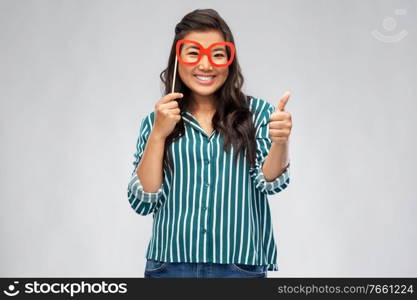 party props, photo booth and people concept - happy asian young woman with big glasses showing thumbs up over grey background. asian woman with party glasses showing thumbs up