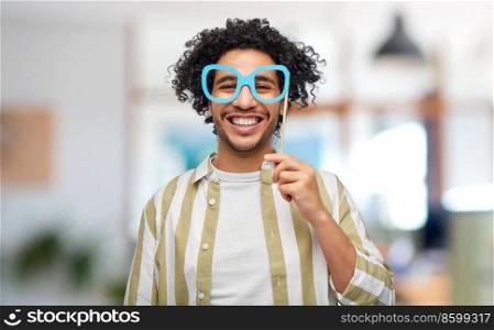 party props, photo booth and people concept - happy smiling young man with paper glasses over office background. smiling man with glasses party accessory at office