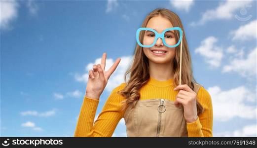 party props, photo booth and people concept - smiling red haired teenage girl with big glasses over blue sky and clouds background. smiling teenage girl with big glasses over sky
