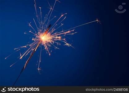 Party sparkler burning bright with sparks on blue background with copy-space.