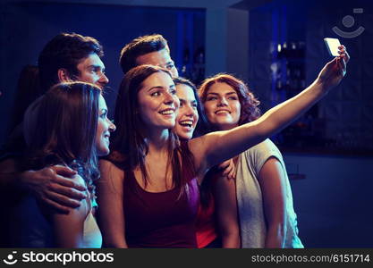 party, technology, nightlife and people concept - smiling friends with smartphone taking selfie in club