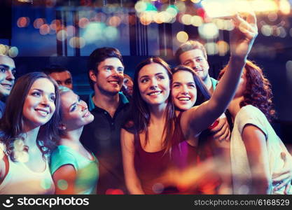 party, technology, nightlife and people concept - smiling friends with smartphone taking selfie in club