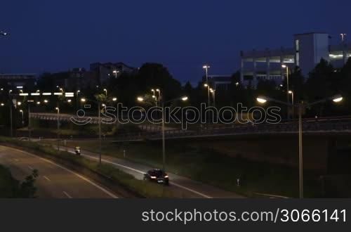 Passenger aircraft approaching for landing at night. Wide shot with highway, cars and airport buildings.