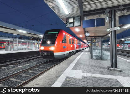 Passenger high speed train on the railway station at night in Europe. Urban landscape with modern commuter train on the railway platform with illumination. Intercity vehicle. Railroad travel. Passenger high speed train on the railway station at night in Europe