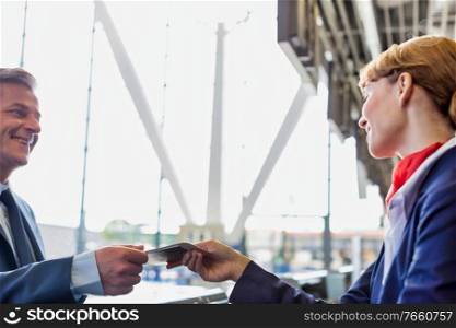 Passenger service agent giving boarding pass to mature attractive businessman after check in at airport