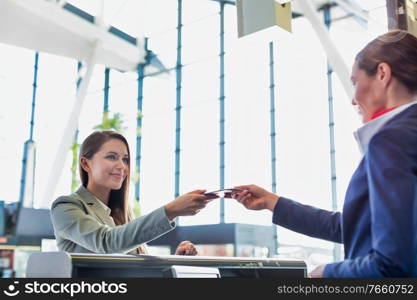 Passenger service agent giving boarding pass to young attractive businesswoman after check in at airport