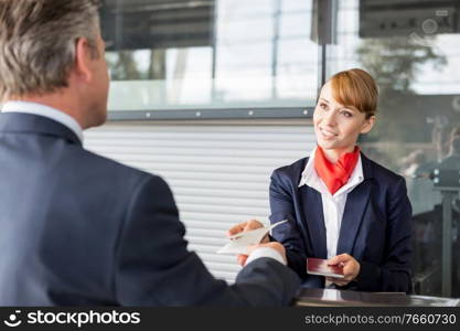 Passenger service agent giving businessman passport and boarding pass in check in area at airport