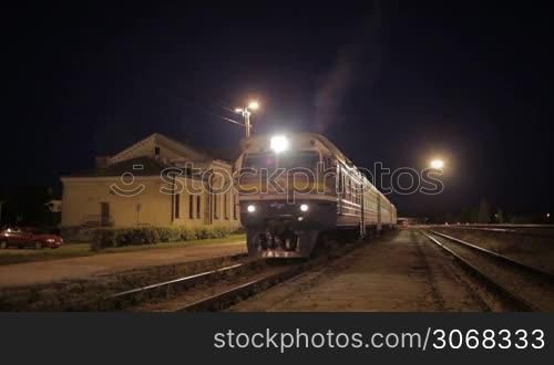 Passenger train leaving small rural station at night.