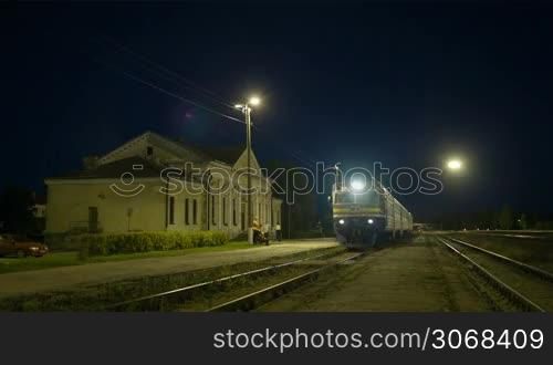 Passenger train making a stopover at a small rural station at night, engine driver leaving cabin to check the train.