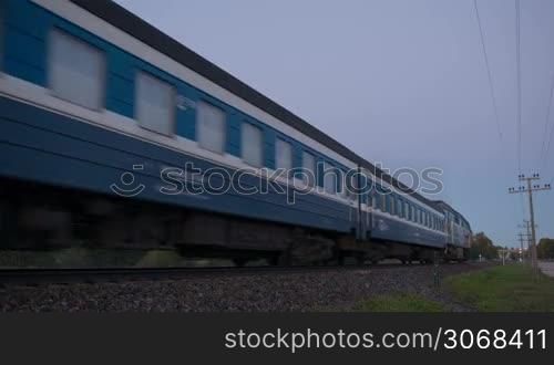 Passenger train passing by slowly in the countryside at sunset.