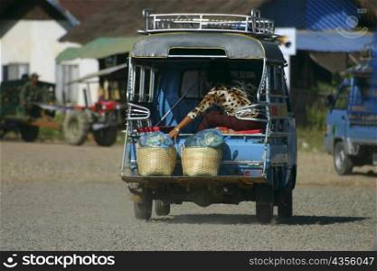 Passenger traveling in a jinrikisha, Vang Vieng, Laos