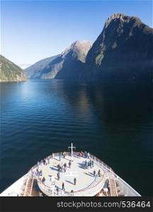 Passengers on cruise ship sailing into Milford Sound on South Island of New Zealand in early morning as the sun rises above the mountains. Fjord of Milford Sound in New Zealand