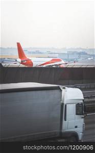 Passengers plane and cargo truck moving side by side. White and red airplane on a runway near a truck on the highway. Fast traveling concept, Germany