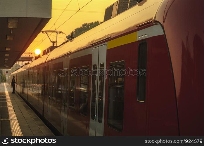 Passengers train side view waiting in the station at sunrise. Sun behind the red train and the modern station platform