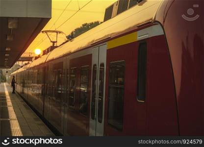 Passengers train side view waiting in the station at sunrise. Sun behind the red train and the modern station platform