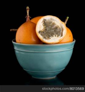 Passion fruit maracuja granadilla on ceramic blue bowl, black background.