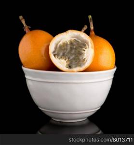 Passion fruit maracuja granadilla on ceramic white bowl, black background.