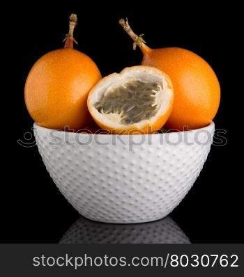 Passion fruit maracuja granadilla on ceramic white bowl, black background.